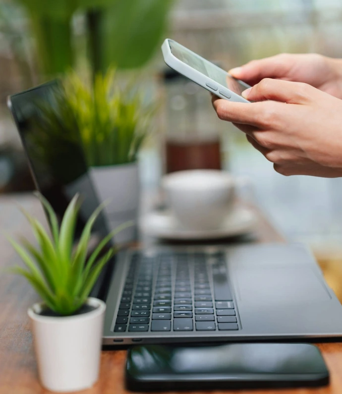 Contact us Person uses phone near laptop on table.